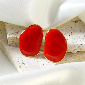 Détail de boucles d'oreilles ovales en émail rouge et bordure dorée sur fond de pierre