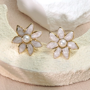 Vista macro detallada de pendientes de flor dorados con perlas y detalles de esmalte