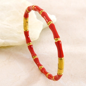 Détail d'un bracelet en acier inoxydable émail rouge et or en forme de bambou sur pierre