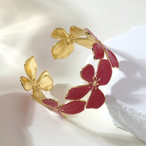 Detailed macro view of golden stainless steel floral cuff with red enamel petals on stone