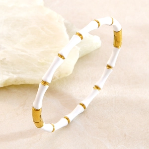 Détail d'un bracelet bambou en émail blanc et or sur un fond de pierre naturelle