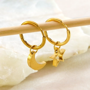 Close-up of golden stainless steel hoop earrings with star and moon charms on stone