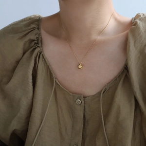 Detailed view of a minimalist gold star pendant necklace worn over a green fabric top