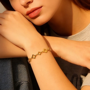 Nahaufnahme eines goldenen Kleeblatt-Armbands, getragen von einem Modell im Sonnenlicht