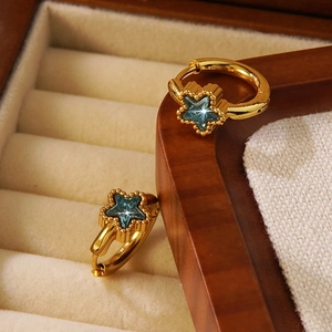Franse gouden oorringen met een blauwe ster edelsteen hanger op een sieradendoosje