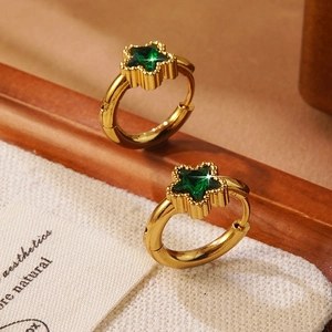 Detailopname van gouden ster oorbellen met groene zirkoon op witte textuur stof
