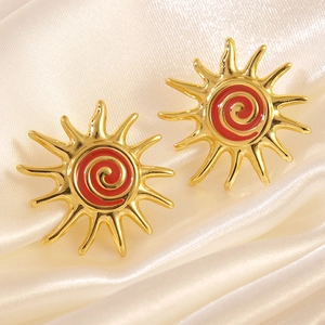Elegant gold-plated sunburst stud earrings with red enamel spiral on silk background