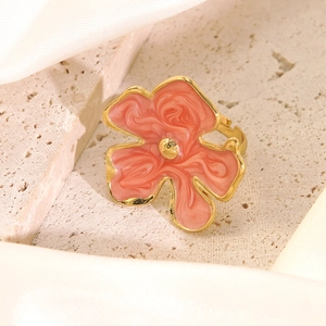 Close-up of golden floral ring with pink marble enamel detail on a soft silk background