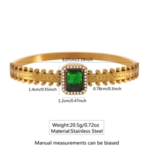 Detail of gold stainless steel bangle with emerald zircon and ornate filigree patterns