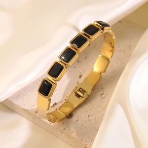 Detailed macro view of gold-plated stainless steel bangle with emerald-cut black stones