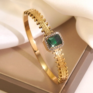 Detailed close-up of a gold-plated vintage bangle with emerald-cut green stone and diamonds