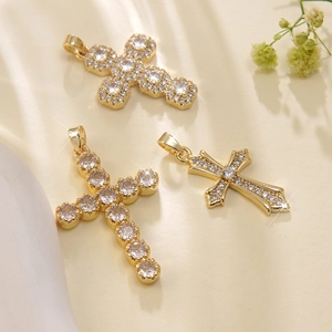 Three gold stainless steel cross pendants with zircon stones on a beige background