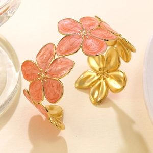 Dettaglio macro del bracciale rigido dorato a forma di C con fiori in smalto corallo