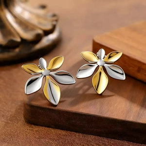 Détail des boucles d'oreilles fleurs bicolores or et argent sur support en bois foncé