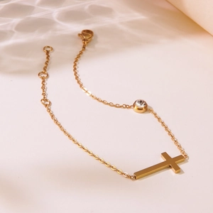 Detail eines Goldkreuz-Armbands mit Zirkon-Stein und verstellbarer Kette auf Wellenhintergrund