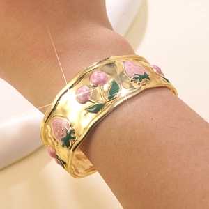 Dettaglio di un bracciale dorato largo con motivi di fragole e ciliegie in smalto