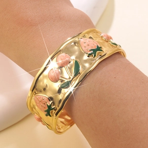 Dettaglio di un bracciale a polsino dorato con texture martellata e motivi di frutta smaltati