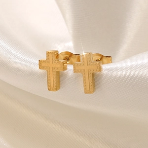 Élégantes boucles d'oreilles croix en acier inoxydable doré sur un fond en satin blanc