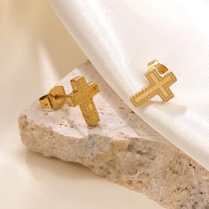 Gros plan de boucles d'oreilles croix dorées texturées sur fond de pierre neutre
