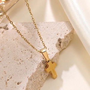 Collier croix en acier inoxydable plaqué or poli posé sur pierre et soie blanche