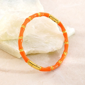 Detail eines orangefarbenen Bambus-Armbands mit polierten Goldmetall-Akzenten