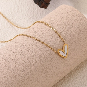 Detailed close-up of a heart-shaped pendant necklace in 18k gold finish with white inlay