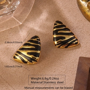 Détail macro de boucles d'oreilles triangulaires en acier avec émail zébré doré et noir