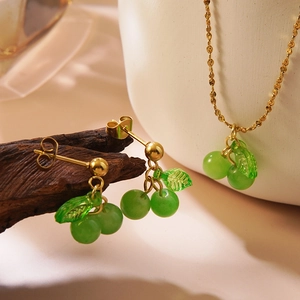 Golden stainless steel cherry jewelry set with green beads on a rustic wooden display