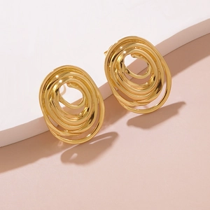 Detail of gold spiral earrings with polished finish on a white geometric stand