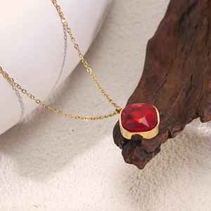 Detail of a square red gemstone pendant on a gold chain over ceramic and wood