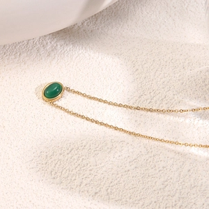 Macro detail of a gold link chain with an oval green cat-eye gemstone pendant