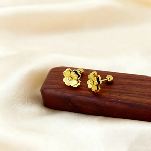 Elegant gold flower stud earrings in matte finish on a premium walnut display stand