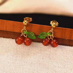 Exquisite cherry stud earrings with red translucent spheres and green leaf on wood stand