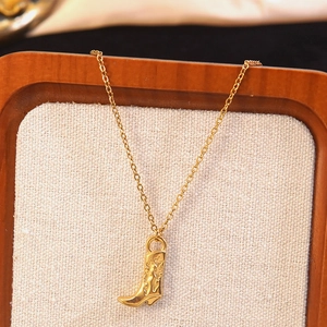 Vintage gold cowboy boot pendant necklace with intricate engraved details on burlap stand