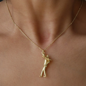 Dettaglio della collana dorata con ciondolo abbraccio sulla clavicola lucida