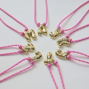 Macro detail of colorful rhinestone inlaid 3D gold initial letters on pink braided cords