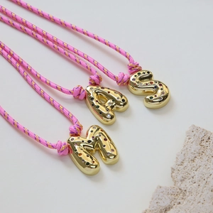 Close-up of golden bubble initial necklaces S A M with colorful gems and pink braided cord