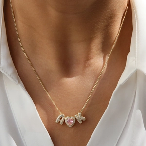 Primo piano della collana con lettera dorata con pietra a cuore rosa e cristalli su modella