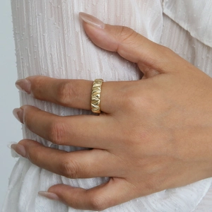 Detail view of gold geometric wide ring featuring textured shell-like wave relief patterns