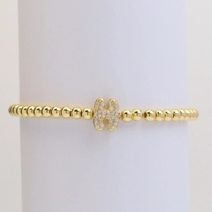 Golden beaded bracelet featuring a micro-pave crystal letter H charm on white stand