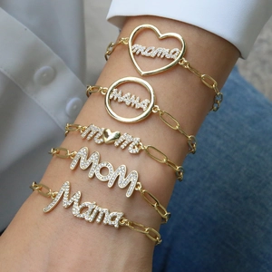 Close-up of golden paperclip bracelets with Mama and Mom zircon pendants on a model's wrist