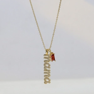 Gold Mama pendant necklace with clear crystals and red birthstone on a minimalist background