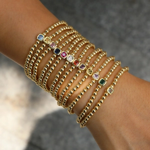 Pulseras de cuentas doradas apiladas con piedras de nacimiento cuadradas de colores