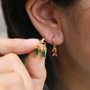 Elegant gold earrings featuring rectangular emerald birthstones shown on model's ear