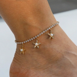 Detailed view of gold anklet with sparkling zircons and delicate pearl star charms