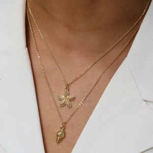 Detail of layered gold necklaces with starfish and conch shell charms on white jacket
