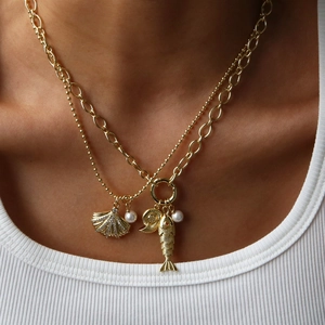 Detail of layered gold necklace with shell, fish, pearl and conch pendants for beach