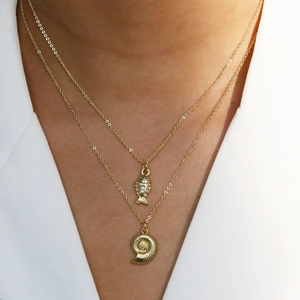 Double layer gold necklace featuring fish and spiral shell pendants on a white blazer