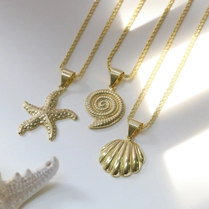 Détail de trois colliers dorés sur le thème marin avec pendentifs étoile de mer et coquillage