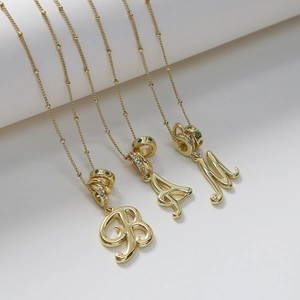 Dettaglio di ciondoli con lettere placcati oro 18k con gemme verdi e pietre di zircone